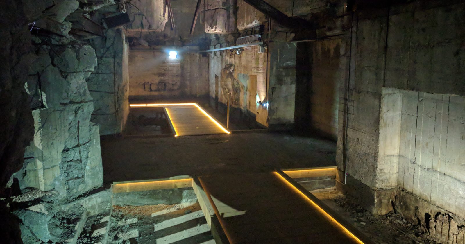 Zniszczone wnętrze betonowego schronu z uszkodzonym stropem i drewnianymi pomostami dla zwiedzających