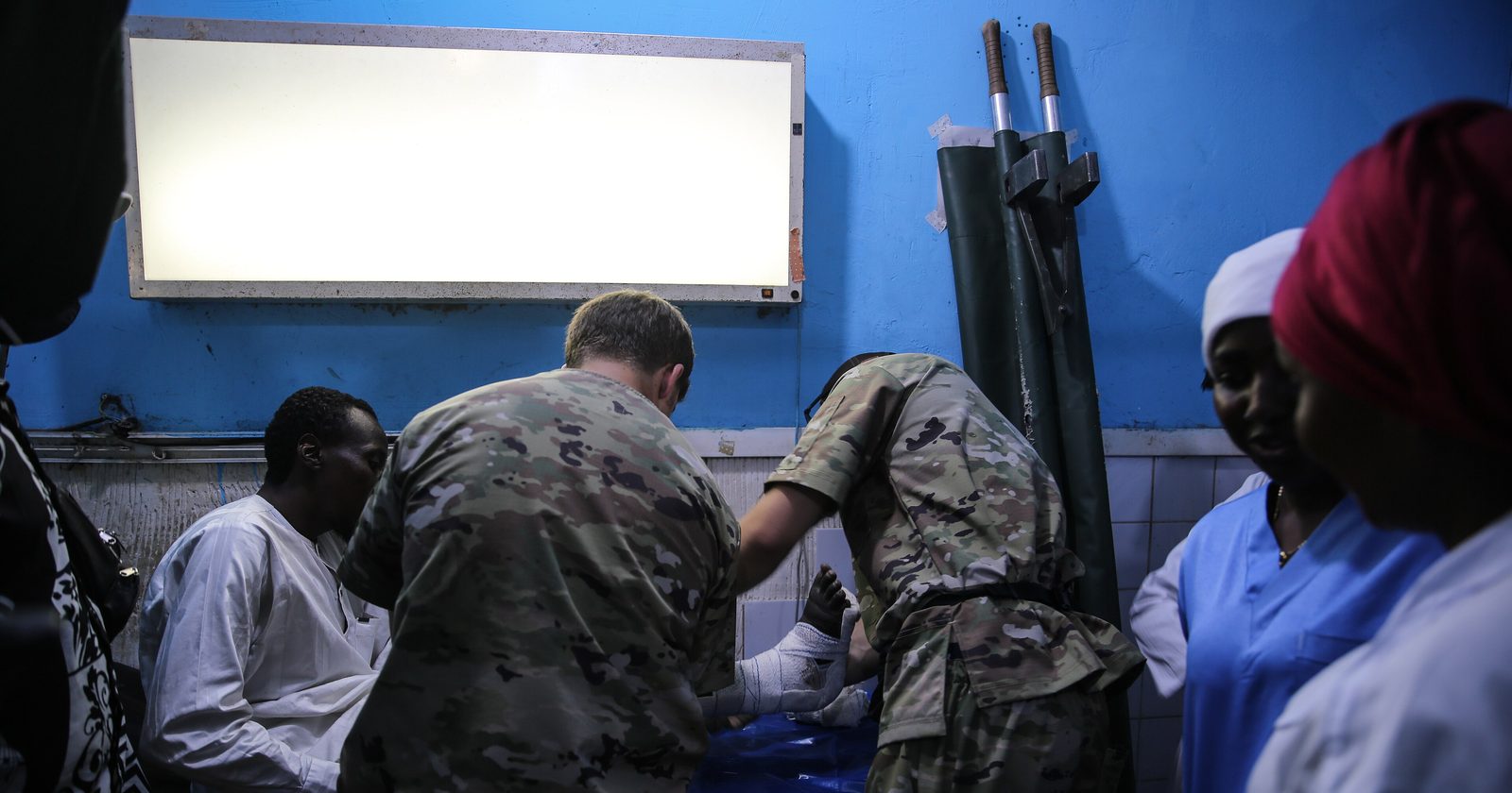 Wojskowi medycy opatrują pacjenta na sali zabiegowej szpitala, obok cywilny personel medyczny