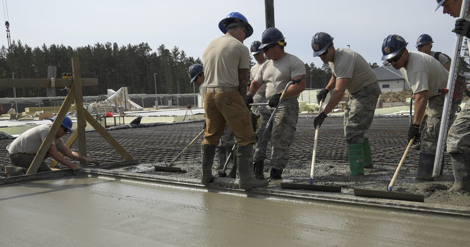 Robotnicy w kaskach wyrównują świeżo wylany beton na zbrojonej płycie fundamentowej budynku