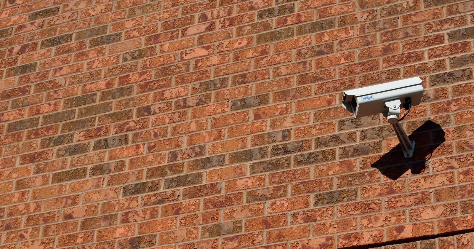Kamera monitoringu zamontowana na ceglanej ścianie budynku.